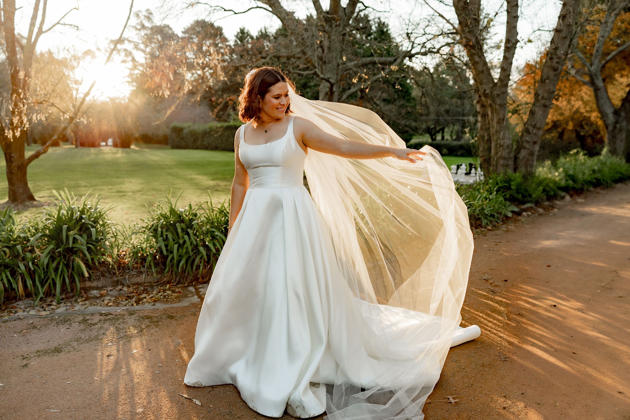 White wedding dress flowing in the breeze along a garden path during sunset.