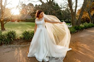 White wedding dress flowing in the breeze along a garden path during sunset.
