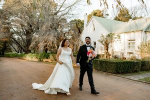 A couple in wedding attire walks together through a scenic outdoor garden setting during their special day.