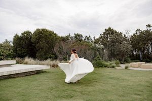 A flowing white wedding dress billows in the wind on a grassy hillside at sunset.