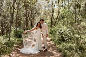 Newlyweds posing on a forest path in elegant wedding attire.