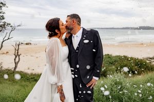 A couple shares romantic kisses in a coastal setting with bubbles floating through the air during their wedding photoshoot.