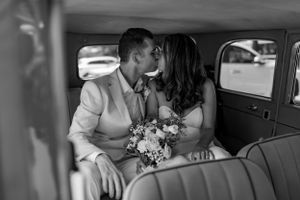 Black and white photo of newlyweds sharing an intimate moment in vintage car.