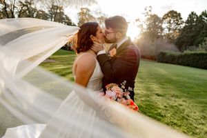 Wedding couple shares intimate moment in golden sunlight with flowing veil catching the breeze.