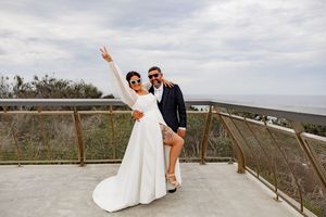 A couple in wedding attire poses for romantic photos on a wooden boardwalk overlooking a scenic coastal landscape.