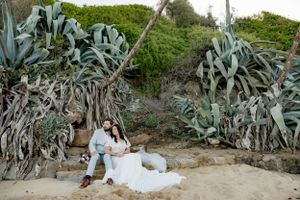 A wedding couple sitting among large cactus plants in a coastal garden setting.
