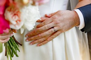 Close-up view of hands holding elegant white and pink wedding bouquets against formal attire.