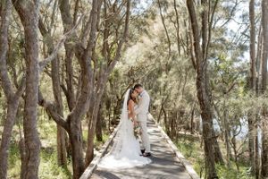 Wedding couple walking along a wooden boardwalk surrounded by tall trees.