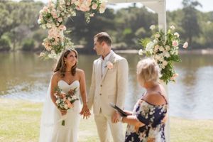 Outdoor waterfront wedding ceremony with floral arch and elegant decor.