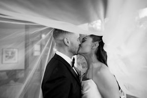Black and white photo of bride and groom sharing a romantic kiss under flowing wedding veil.