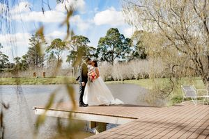 Couple embraces on a wooden dock over a lake with sunlight streaming through trees on a bright autumn day.