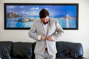 A formal light gray suit being buttoned in front of coastal artwork.