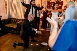 Guests celebrate at a lively wedding reception, with a man kneeling on the dance floor amid cheering crowd.