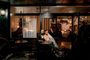 Bride and groom pose together outside elegant wedding venue at night with warm glowing lights.