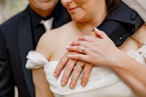 Close up view of hands with wedding rings against white fabric background.