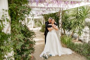 Wedding couple poses in lush garden setting under string lights and tropical foliage.