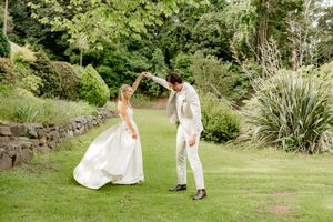 Two people in white outfits dancing together on a lush green lawn surrounded by garden landscaping.