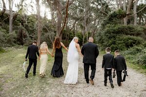 Wedding party walking down a wooded path together wearing formal black and white attire.