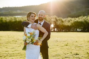 A couple in wedding attire embraces in a sunlit meadow during golden hour photography session.