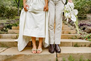 Close-up details of wedding attire and bare feet on stone garden steps with greenery.