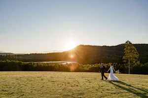 Silhouetted couple in wedding attire stand together in a golden field at sunset with mountains in the background.