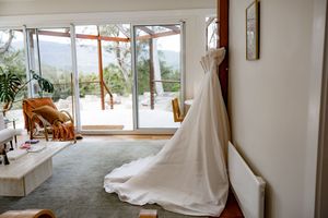 White curtains billow in a bright sunlit room with large windows overlooking a scenic mountain landscape.
