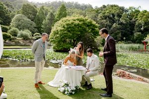 Wedding ceremony taking place on a lush green lawn with garden scenery in the background.