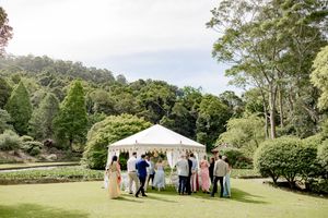 Panoramic view of an outdoor wedding ceremony setup with a white tent and guests gathered on a lush green lawn.