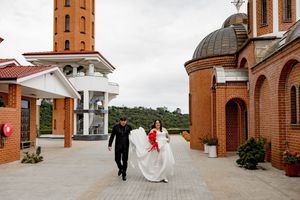 Red brick church exterior with arches and domed tower shown in panoramic view.