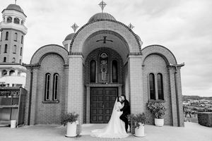 White stone Orthodox church exterior with domed towers and crosses shown in panoramic view.