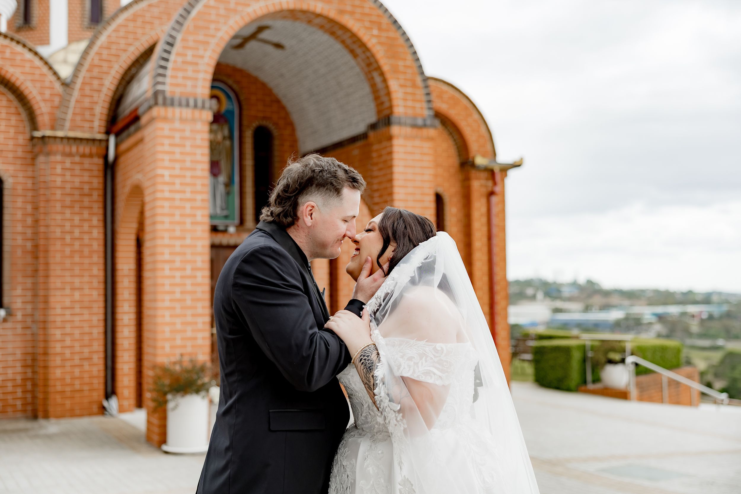 Wedding couple embracing outside a brick church with arched architecture.