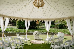 A white wedding tent with elegant draping and geometric pendant lights set up for an outdoor celebration.