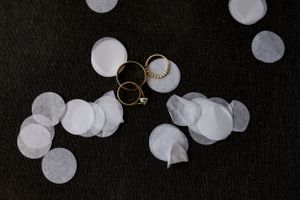 Wedding rings arranged artistically among white confetti on dark background.