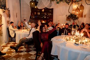 Wedding reception guests raising glasses in a toast at candlelit tables in a decorated venue.