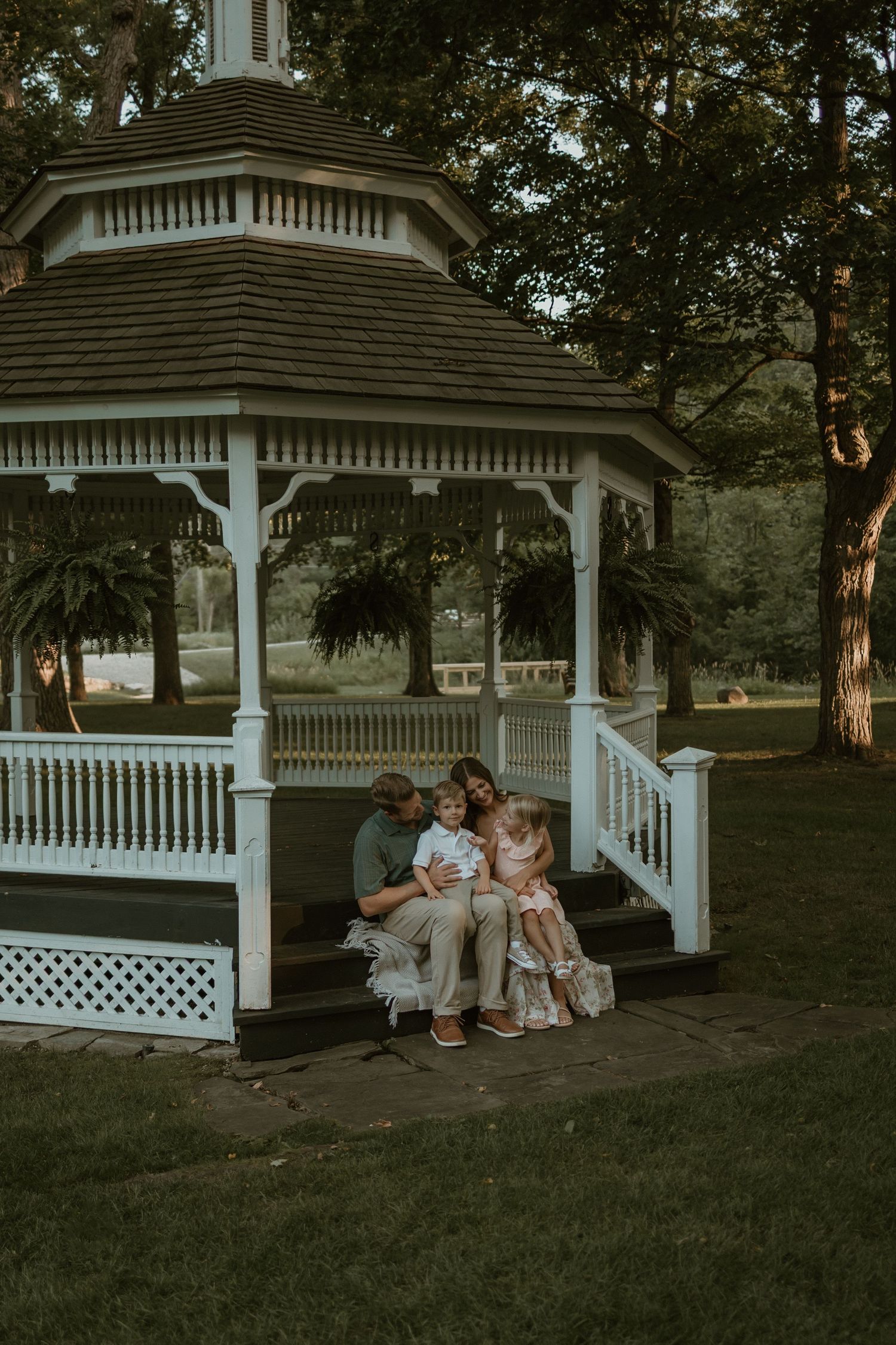 Two young children stand together in a sunlit garden with flowers during golden hour.