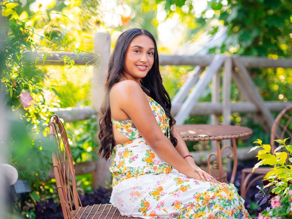 Floral white dress photographed in natural garden setting with wooden fence backdrop.