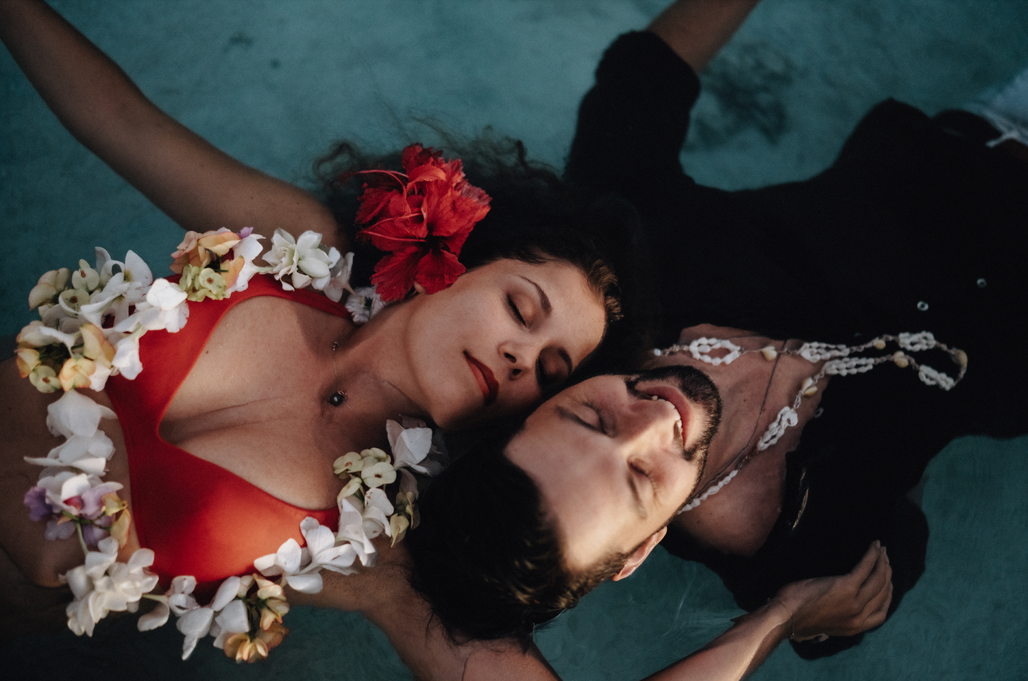 Underwater-style portrait with red swimwear and floating floral arrangements.