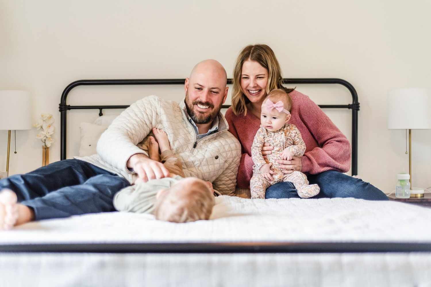 Family relaxes together on a black metal bed frame while enjoying a playful moment at home.