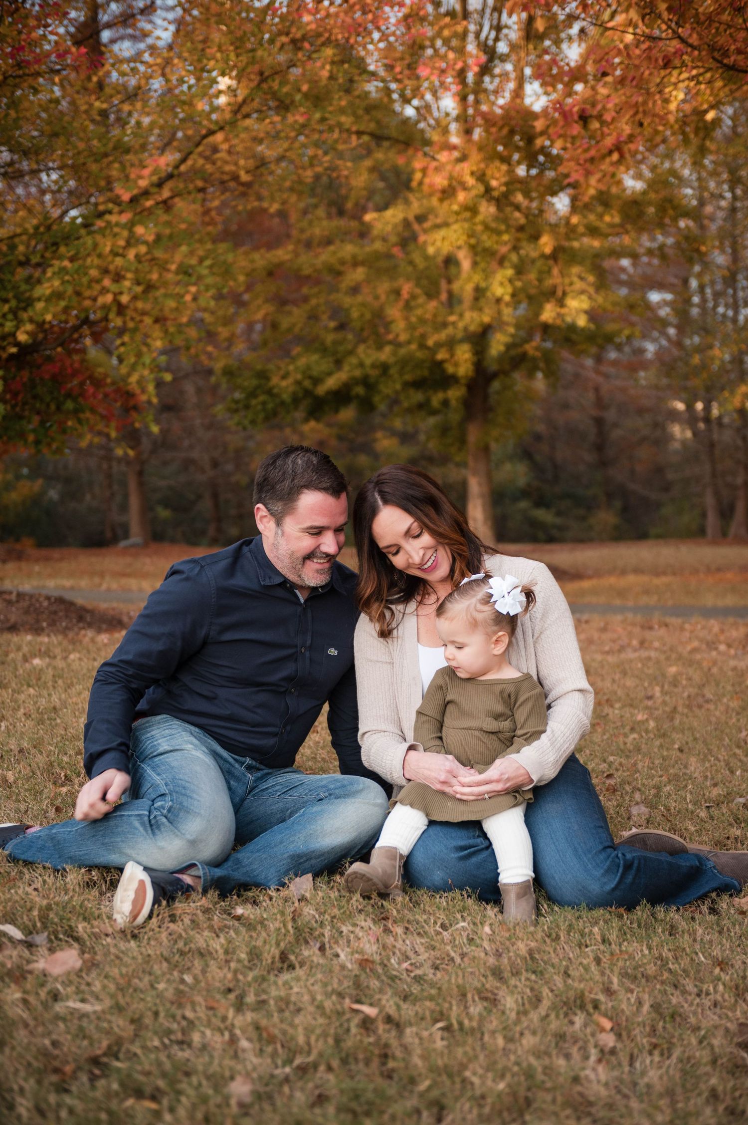 Family lounging together on autumn grass with golden fall foliage in background.