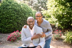 Couple sharing a tender moment near flowering bushes in garden setting.