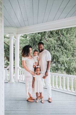 A sweet family photoshoot on a white porch with everyone wearing coordinating white outfits.