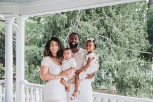 Bright outdoor family portrait session on white porch with natural greenery.