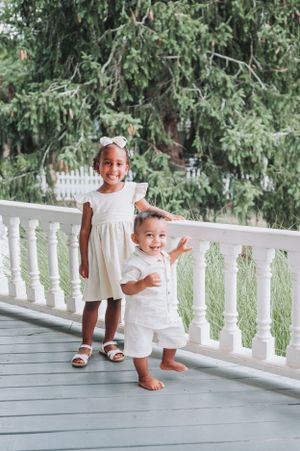 Children playing and posing on a white porch with rustic balustrades.