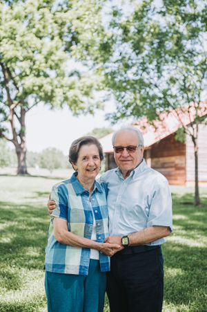 Senior couple embracing and smiling together in a sunny park with trees in the background.