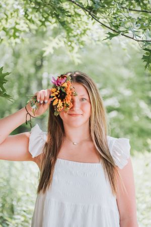 Woman in white dress playfully posing with orange flowers against leafy green background.