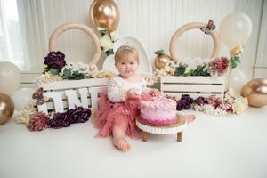 Decorated cake smash photo setup with pink cake, balloons, and floral accents.