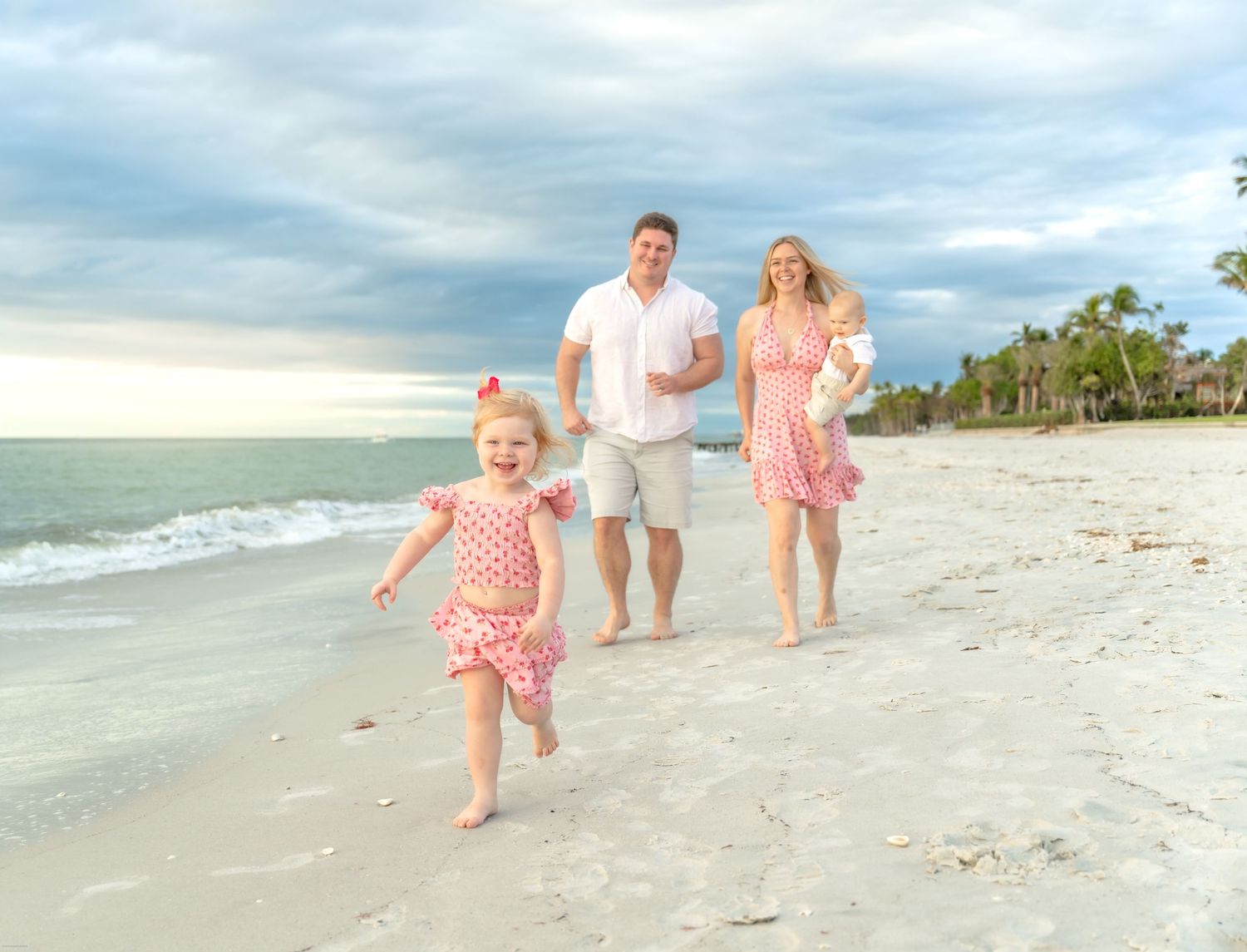 A family walking along a pristine beach at sunset with waves in the background.