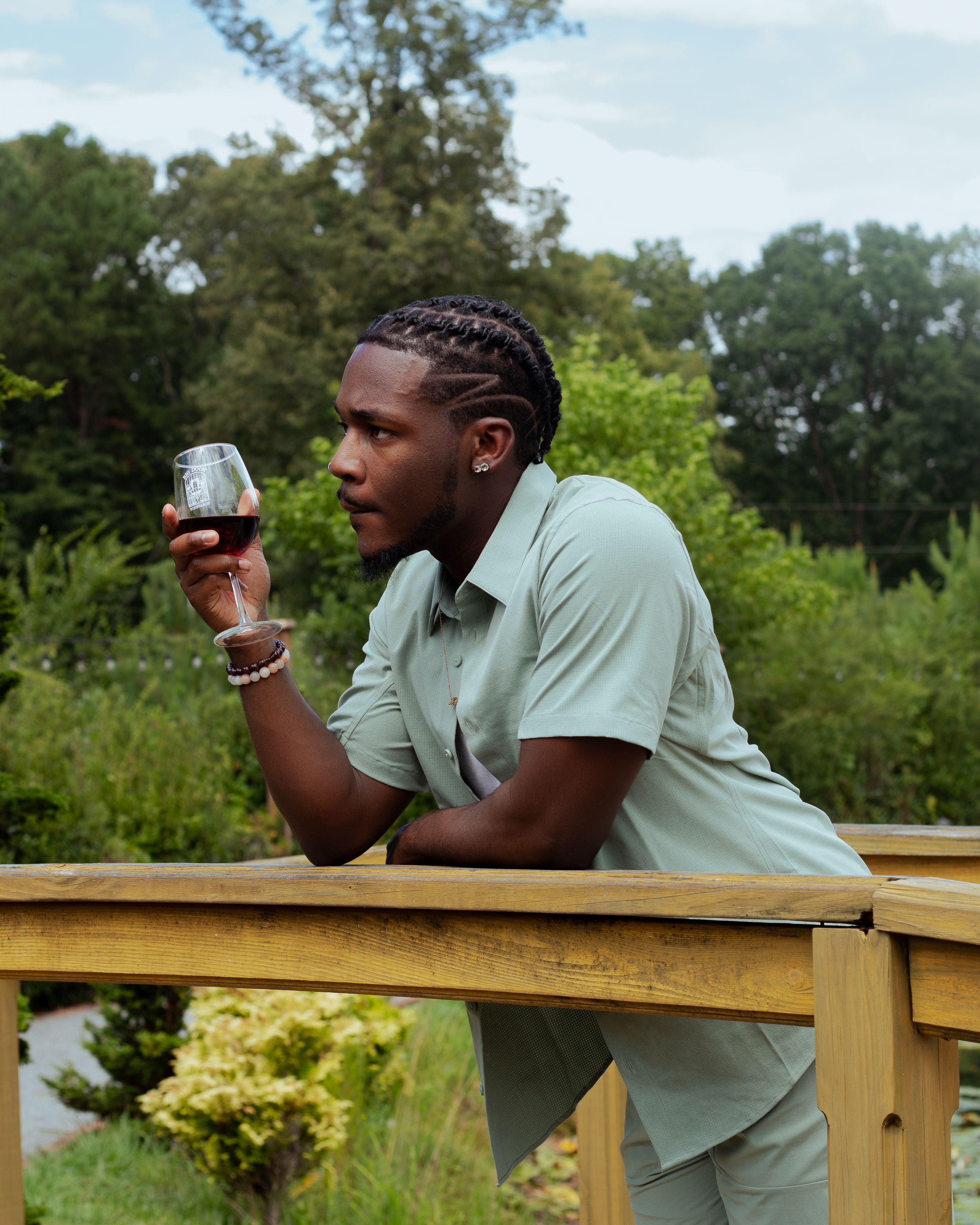 Person in mint green shirt examining wine glass on wooden deck.