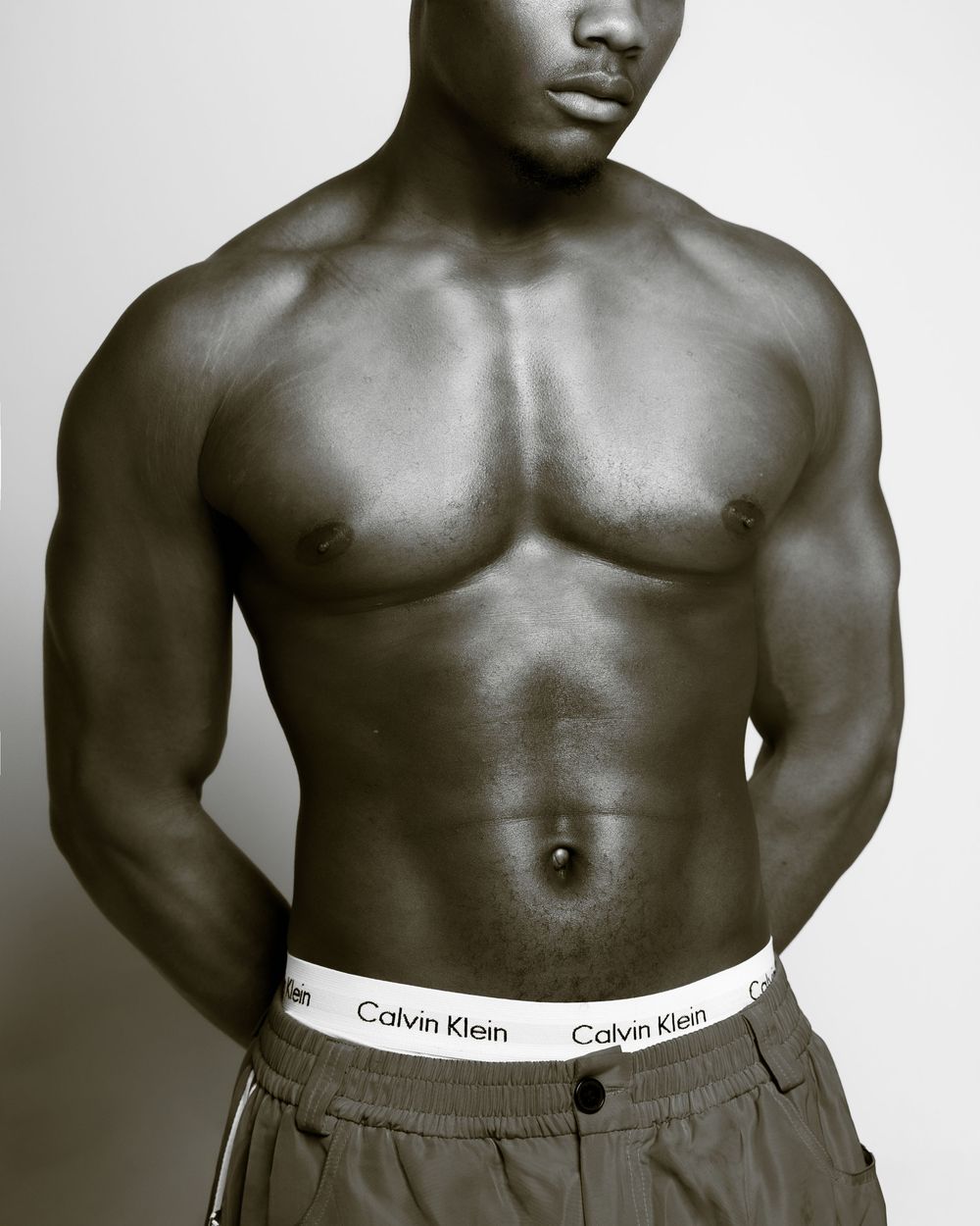 Black and white fashion photograph showing muscular torso wearing Calvin Klein underwear waistband and casual pants.