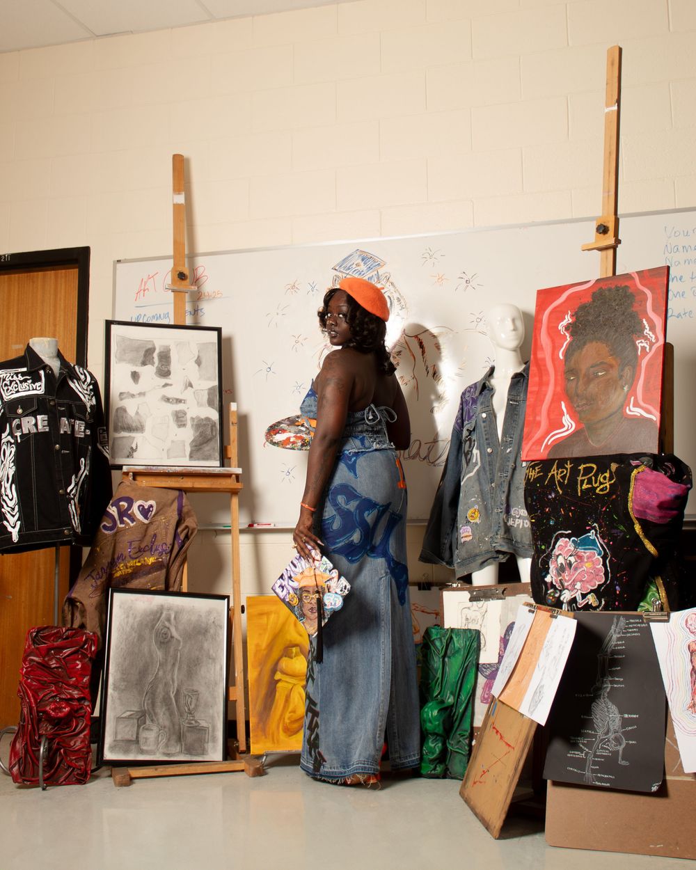 Art gallery wall displays multiple paintings and sketches arranged on wooden easels against a beige wall.